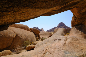 View from inside the Spitzkoppe arch in Damaraland, Namibia, showcasing smooth granite formations under a clear sky.