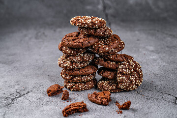 Stack of rich chocolate cookies with sesame seeds, presented on a textured surface