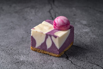 Blueberry and Cream Cheesecake Square with a Marbled Design and Decorative Pink Sphere on a Cracked Stone Surface