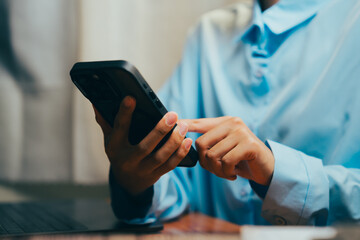 Person using smartphone while sitting at a table with laptop in a cozy indoor setting, Business concept.