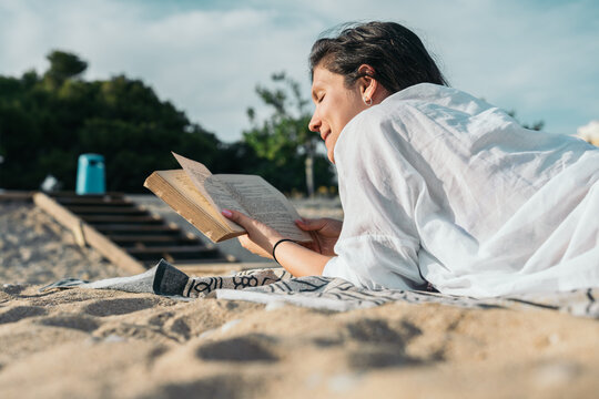 Young woman relaxing on the beach reading a book