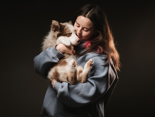 Obraz premium A young woman holds a small border collie puppy in her arms. She loves and adores him. The background is dark.