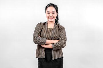 An Indonesian woman wearing traditional lurik attire smiles confidently with her arms crossed,...