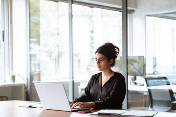 Young professional it specialist latin hispanic business lady working on laptop pc sitting at desk...