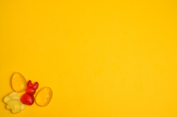 Bright yellow and red gummy candies shaped like Easter bunnies, eggs, and carrots are neatly placed in the lower-left corner on a vibrant yellow background. Ideal for festive design projects.