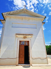 Small white chapel with wooden door under a bright blue sky