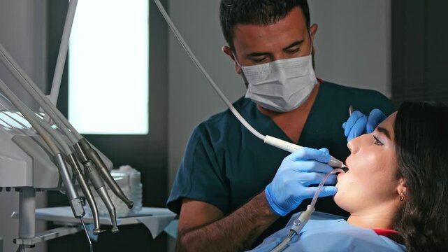 Professional dentist treating a patient in a modern clinic. The patient sits with an open mouth as the dentist drills and cleans teeth with water, ensuring proper dental care and hygiene.