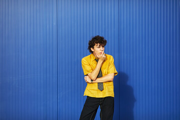 Young student pondering against a vibrant blue wall in an urban setting during daylight hours