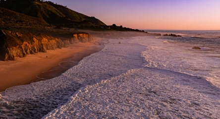 Beautiful sunset over the Big Sur beach with waves crashing on the shore.  Two people walking on the beach