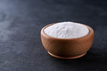 salt in a wooden bowl on a black stone table, selective focus.