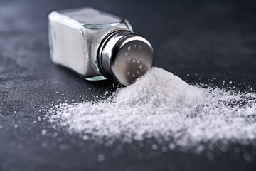 glass salt shaker  and crystals of salt on a black table.