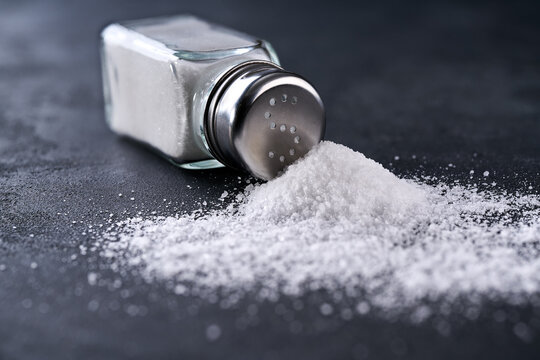glass salt shaker  and crystals of salt on a black table.