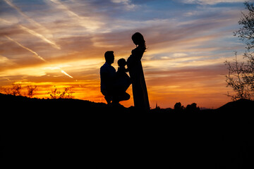 silhouette of a man standing in front of the sunset with child and pregnant wife