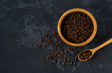 Wooden bowl with cloves spice on a black kitchen table, top view.