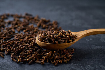 cloves spice in a wooden spoon on a black stone table, selective focus.