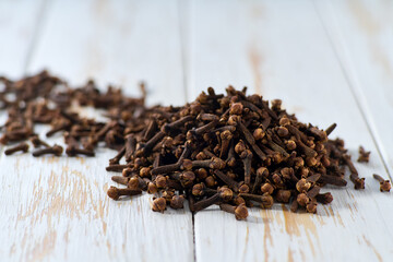 Pile cloves spice on a white wooden table, selective focus.