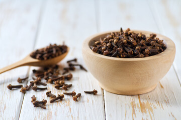 cloves spice in a wooden bowl on a light kitchen table,  selective focus.
