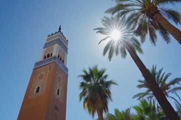 Tall terracotta minaret under sunny sky, flanked by palm trees.