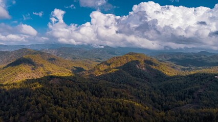 Aerial view of lush green mountains under a partly cloudy sky.