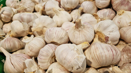 Garlic close up in supermarket. Lots of garlic in plastic green box on market stall. Garlic in green plastic box at farmers market. Garlic for sale in store. Display of fresh produce for sale