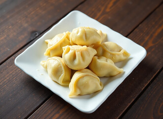 Close-up overhead shot of several light yellow dumplings on a white square plate, set against a dark brown wooden background.