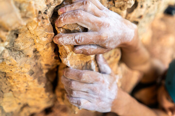Young girl is engaged in extreme sports, fearlessly climbs up the rock using white magnesia powder, holds her hand to the ledge in the relief,