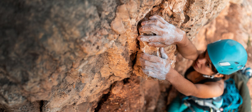 Young girl is engaged in extreme sports, fearlessly climbs up the rock using white magnesia powder, holds her hand to the ledge in the relief,