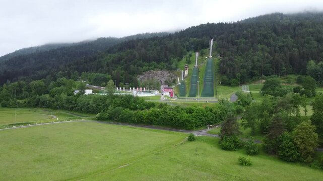 Ski jumps at villacher alpen arena. Drone aerial view of ski jumps at villach in spring, green grass and no snow. overview with camera zooming in or panning