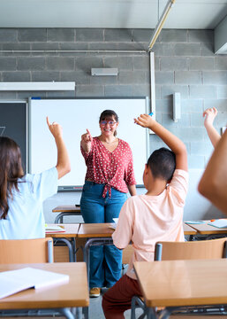 Vertical. Excited group diverse elementary school students sitting in classroom attending by raising hands. Hispanic pre-teens children answering teacher question in class. Primary school concept