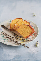 Easter cake sliced ​​of cake on a plate, with a fork and willow branches with catkins, minimalist composition on a muted gray-blue background, close-up.