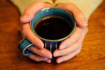 温かいコーヒーの入ったマグカップを持つ女性の手元