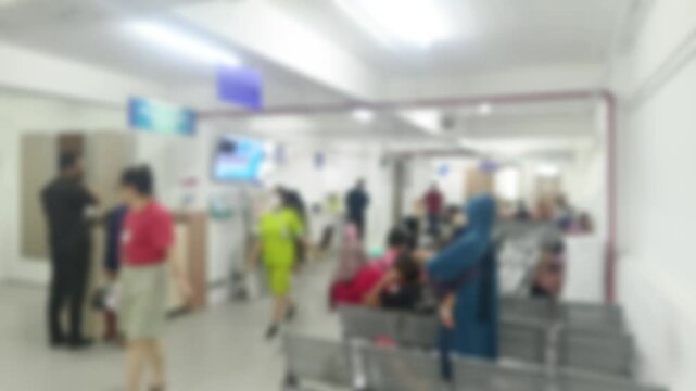 An intentionally blurred image showing a diverse crowd in a waiting room setting. The soft focus creates a sense of anonymity, underscoring the universal experience of seeking medical assistance.