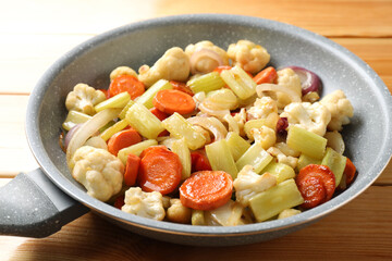 Frying pan with vegetables on wooden table, closeup