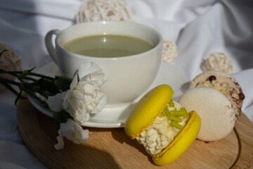 Green latte matcha with yellow and white sweet macaron on messy bed. Concept of holiday breakfast morning tea drink. Cozy minimalist superfood vibrant colors healthy eating. Organic caffeine-free