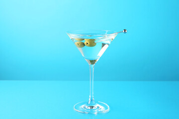 Martini cocktail with olives in glass on light blue background