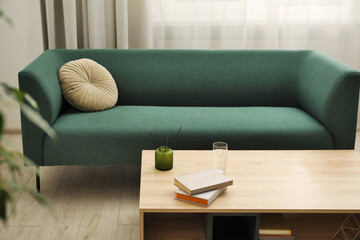 Books, glass of water and reed diffuser on wooden coffee table near sofa in living room, space for...