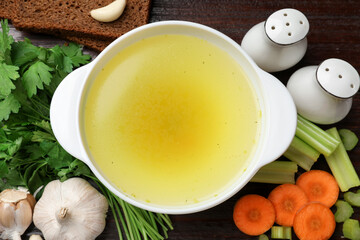 Tasty chicken bouillon in bowl with bread and ingredients on wooden table, flat lay