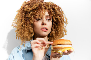 Young woman with curly hair contemplating a burger, showcasing emotions of curiosity and hesitation...