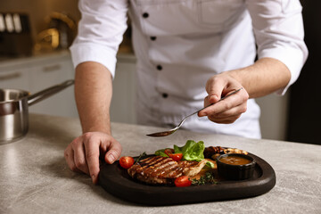 Professional chef adding sauce to delicious dish at table indoors, closeup