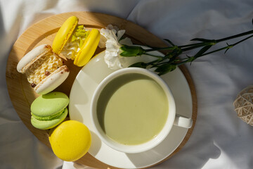 Green latte matcha with yellow and white sweet macaron on messy bed. Concept of holiday breakfast morning tea drink. Cozy minimalist superfood vibrant colors healthy eating. Organic caffeine-free