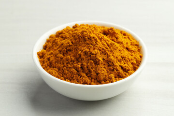 Turmeric powder in bowl on white table, closeup