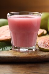 Tasty guava juice in glass, leaf and fruits on wooden table, closeup