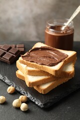 Sandwich with chocolate butter and hazelnuts on black table, closeup