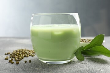 Fresh mung bean juice in glass, seeds and green leaves on grey table, closeup