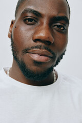 Obraz premium Portrait of a young man with a confident expression, wearing a white t shirt, against a neutral background, showcasing a blend of modern style and natural charisma