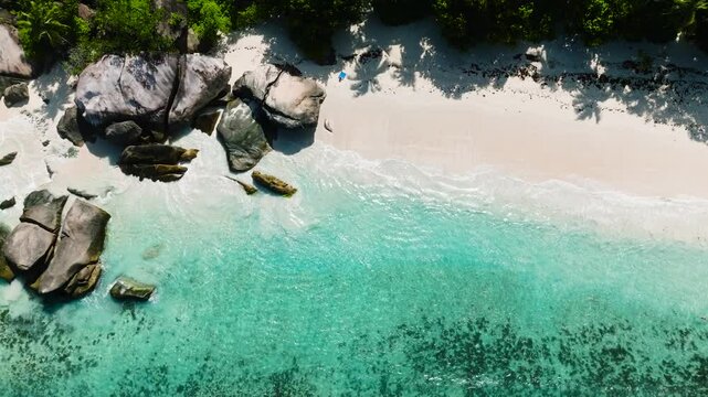 Rock formations stand along the edge of a turquoise sea meeting sandy beach. Seychelles, Mahe. Roche Copra.