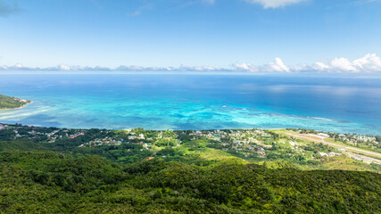Vibrant green hills extend toward the horizon, meeting the bright turquoise sea under a clear blue sky. Praslin, Seychelles.
