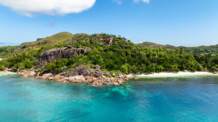 Cove with granite boulders, sandy beach, and lush green hills bordering the coast. Curieuse, Seychelles.