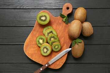 Board with slices of fresh kiwi and mint on black wooden background