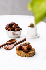 Portrait image of delicious sweet dates, sweet dried dates fruit popular during Ramadan, typical fruit of fasting month. served on white table with ornamental plants, wooden spoon and fork